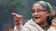 Die Ministerpräsidentin von Bangladesch, Sheikh Hasina, hat ihren Zeigefinger ausgestreckt. Sie trägt eine Brille und ein Kopftuch. © Rajesh Kumar Singh/AP/dpa Foto: Rajesh Kumar Singh/AP/dpa