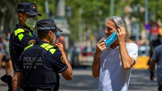 Polizisten weisen einen Mann in Spanien darauf hin, einen Mund-Nasen-Schutz zu tragen. © dpa Foto: Emilio Morenatti