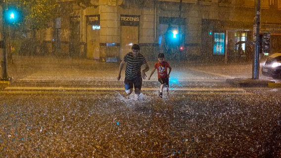 Menschen überqueren in Pamplona in Spanien bei starkem Regen eine überschwemmte Straße. © AP/dpa-Bildfunk Foto: Alvaro Barrientos