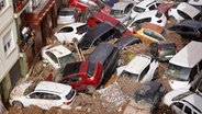 Valencia: Anwohner betrachten durch die Wassermassen aufgestapelte Autos. © Alberto Saiz/AP Foto: Alberto Saiz