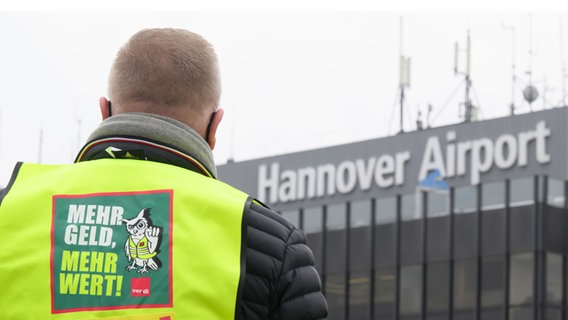 Ein Sicherheits·mitarbeiter steht in gelber Warn·weste vor dem Flughafen in Hannover. © dpa Foto: Julian Stratenschulte