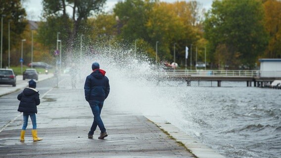 Spaziergänger gehen bei Wellengang und Gischt am Ufer der Kieler Förde entlang. Auch in Kiel sorgte der Oststurm für Hochwasser. © picture alliance/dpa | Gregor Fischer 