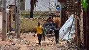 Jugendliche gehen auf einer von Zerstörungen gezeichneten Straße in Omdurman im Sudan. © Mudathir Hameed/dpa 