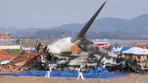 Feuerwehrleute und Mitglieder eines Rettungsteams arbeiten in der Nähe des Wracks eines Passagierflugzeugs am Muan International Airport in Südkorea. © picture alliance/dpa/AP Foto: Ahn Young-joon