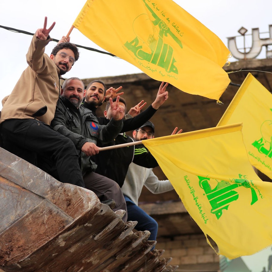 Männer, die in der Schaufel eines Bulldozers sitzen, schwenken Hisbollah-Fahnen, während sie die Waffenruhe zwischen Israel und der Hisbollah feiern, die am Mittwoch (27.11.2024) begonnen hat. © dpa/AP Foto: Mohammed Zaatari