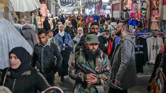 Ein bewaffneter Oppositionskämpfer geht zwischen den Kunden auf dem Al-Hamidiyeh-Markt innerhalb der alten Stadtmauern von Damaskus in Syrien. © dpa-Bildfunk/AP Foto: Hussein Malla