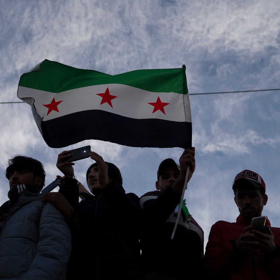 Unter einer syrischen Flagge versammeln sich mehrere Menschen. © dpa Bildfunk Foto: Leo Correa