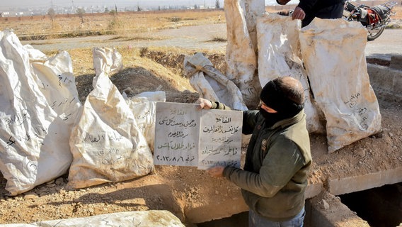 Ein Arbeiter hält ein Schild mit Informationen über den Inhalt eines Massengrabs im Bereich der Bagdad-Brücke außerhalb von Damaskus, Syrien. © picture alliance / Middle East Images | Fadel Itani Foto: Fadel Itani