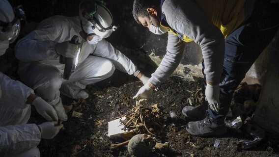 Syrische Zivilschützer sammeln menschliche Überreste ein, die in zwei verschiedenen Kellern in einem Außenbezirk von Damaskus gefunden wurden. © AP/dpa Foto: Omar Albam