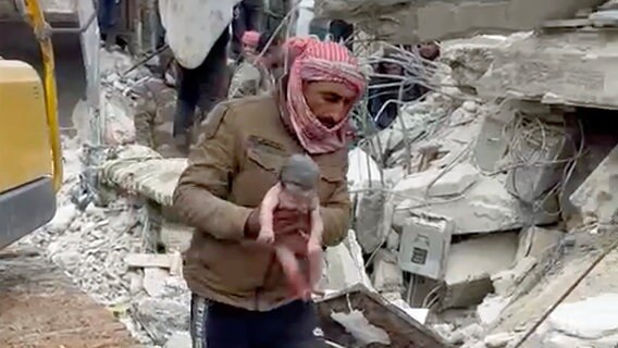 In Jinderis in Syrien trägt ein Retter ein neugeborenes Mädchen, nachdem es aus Trümmern befreit worden ist. © dpa bildfunk/Verified UGC/AP 