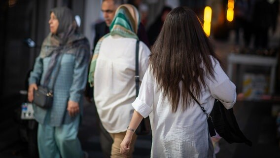 In Teheran laufen mehrere Frauen eine Straße entlang: einige mit Kopftuch, eine Frau ohne Kopftuch. ©  Arne Bänsch/dpa 