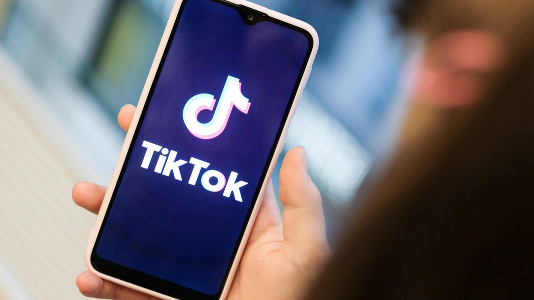 Ein Mädchen hält ihr Smartphone mit dem TikTok Logo in der Hand 