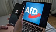 Eine Hand hält ein Smartphone, auf dem die TikTok-App zu sehen ist. Dahinter steht ein Laptop mit dem Logo der AfD. © picture alliance / Sipa USA | PRESSCOV 