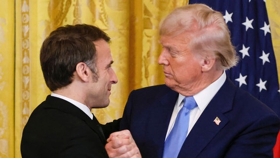 24.02.2025, USA, Washington: US-Präsident Donald Trump (r) und Frankreichs Präsident Emmanuel Macron schütteln sich nach einer gemeinsamen Pressekonferenz im East Room des Weißen Hauses die Hände. © AFP Foto:  Ludovic Marin