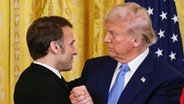 24.02.2025, USA, Washington: US-Präsident Donald Trump (r) und Frankreichs Präsident Emmanuel Macron schütteln sich nach einer gemeinsamen Pressekonferenz im East Room des Weißen Hauses die Hände. © AFP Foto:  Ludovic Marin