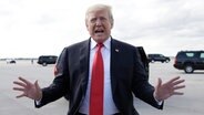 Donald Trump posiert auf einem Flugplatz vor einer Kamera, er trägt Anzug und eine rote Krawatte, er streckt die Arme von sich. © DPA Bildfunk Foto: Kaster, Carolyn