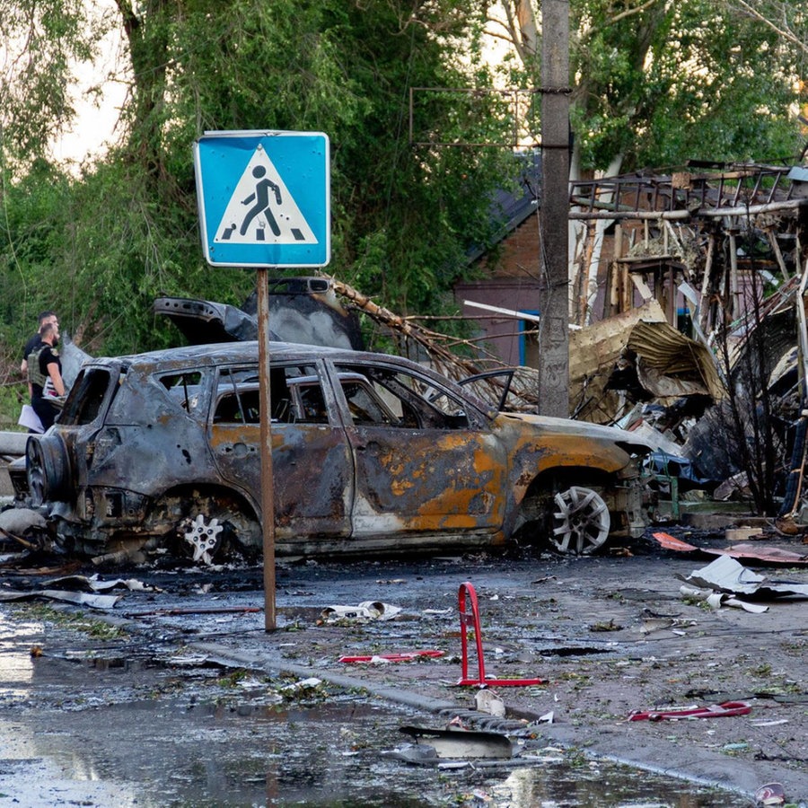 Ein von einer russischen Rakete zerstörtes Auto steht qualmend vor den Trümmern eines Hauses. © picture alliance / Anadolu | Kherson Regional Military Administration of Ukraine / Handout 