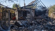 Ein beschädigtes Haus ist im Hintergrund von Fragmenten eines abgeschossenen russischen Militärflugzeugs am Stadtrand von Kostjantyniwka, einer Stadt nahe der Frontlinie in der Region Donezk, zu sehen. © Iryna Rybakova/AP 