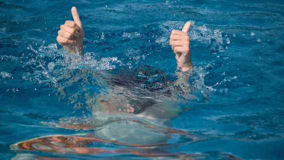 Zwei Daumen recken aus dem Wasser eines Mannes, der gerade untergegangen ist. © ufi100/fotolia Foto: ufi100