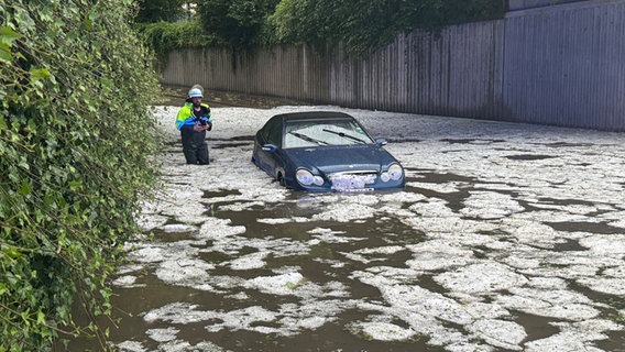 Bayern, Immenstadt: Nach schweren Unwettern steht ein Auto auf einer überfluteten Straße, in der Hagelkörner treiben. © Michael Breher/dpa Foto: Michael Breher