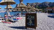 Strandszene mit Sonnnschirmen und Strandliegen in Kroatien mit einem Aufsteller: "20 Euro pro Liegestuhl" © picture alliance / johapress Foto: Joachim Hahne