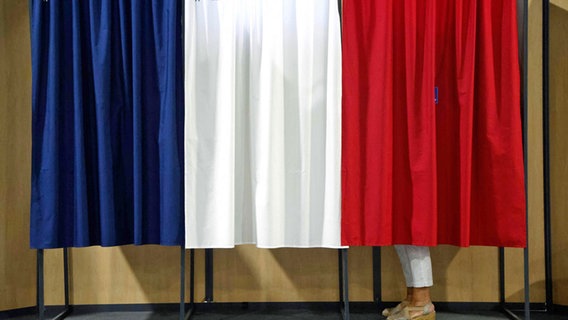Eine Frau steht in einem Wahllokal in einer Wahlkabine, um ihre Stimme für die zweite Runde der französischen Parlamentswahlen abzugeben © AFP/dpa Foto:  Ludovic Marin
