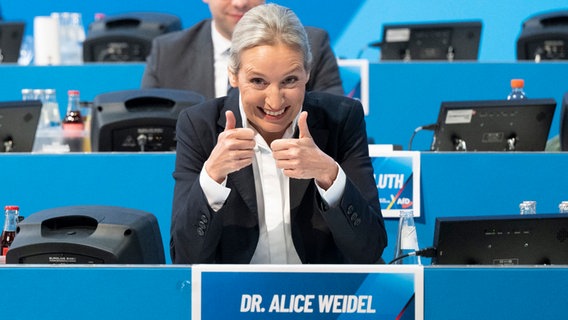 AfD-Kanzlerkandidatin Alice Weidel sitzt beim Parteitag in Riesa auf einem Podium und reckt beide Daumen nach oben. © dpa Foto: Sebastian Kahnert