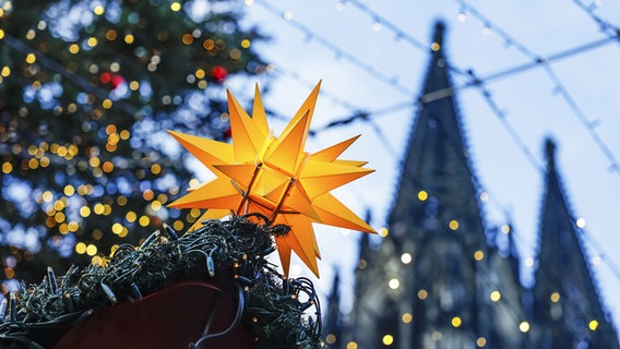 Leuchtender, gelber Stern auf einem Weihnachtsmarkt mit Lichterketten am Kölner Dom. © picture alliance Foto: Jan Tepass