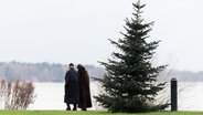 Zwei Spaziergänger gehen hinter einem Weihnachtsbaum am Ufer des Zwischenahner Meeres. © dpa-Bildfunk Foto: Mohssen Assanimoghaddam