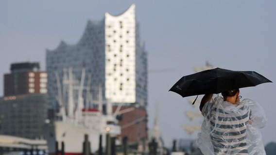 Ein Frau fotografiert nach Starkregen die Hamburger Elbphilharmonie und schützt dabei ihren Fotoapparat mit einem Regenschirm. © dpa-Bildfunk Foto: Bodo Marks/dpa