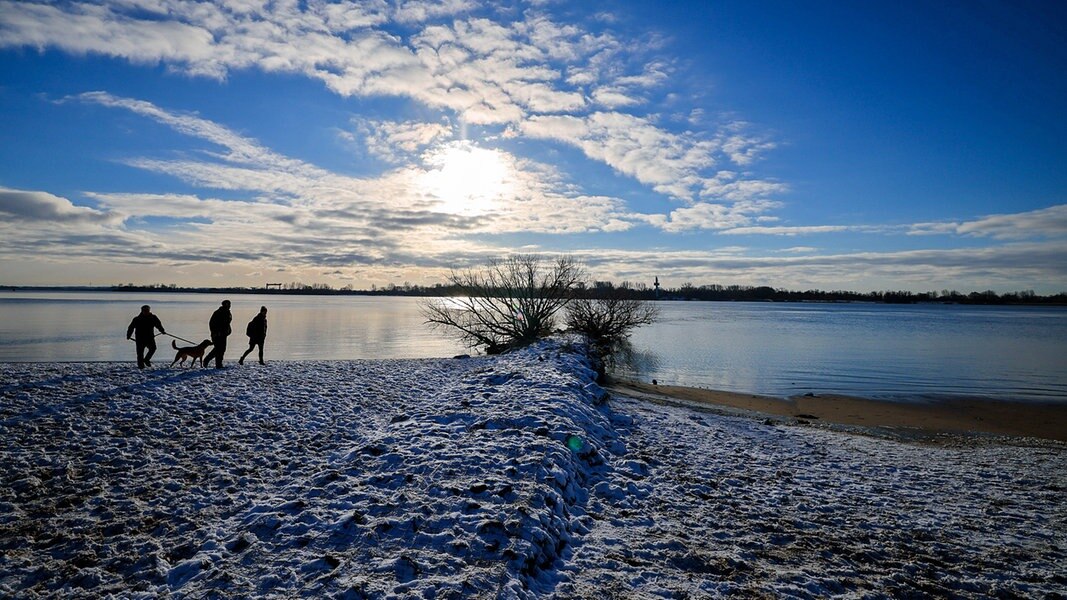 Menschen sind bei sonnigem Winterwetter am schneebedeckten Elbstrand des Falkensteiner Ufers bei Hamburg-Blankenese unterwegs.