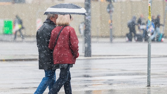 Ein Mann und eine Frau gehen mit einem Regenschirm bei Schneeregen (Archivbild) © Christophe Gateau/dpa Foto: Christophe Gateau