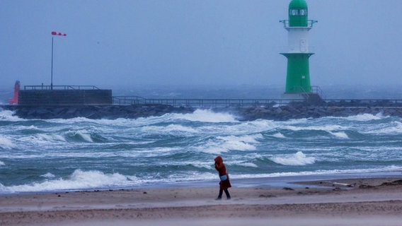 Eine Frau geht bei Sturm und Regen über den Strand an der Ostseeküste in Warnemünde. © picture alliance/dpa | Jens Büttner 