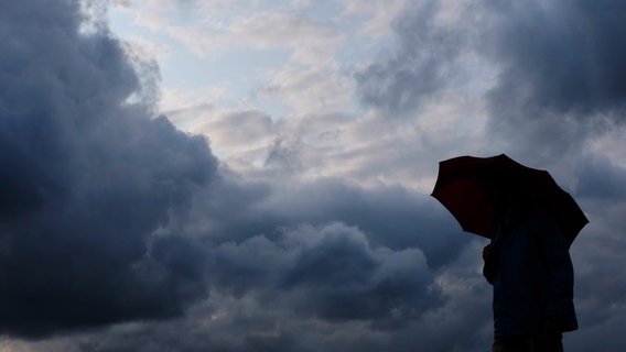 Ein Mann geht mit einem Regenschirm vor aufziehenden dunklen Wolken spazieren. © Martin Gerten/dpa Foto: Martin Gerten