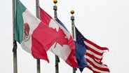 Die Flaggen von Mexiko, Kanada und den USA sind in der Nähe der Ambassador Bridge in Detroit, Michigan zu sehen. © Paul Sancya/AP/dpa 