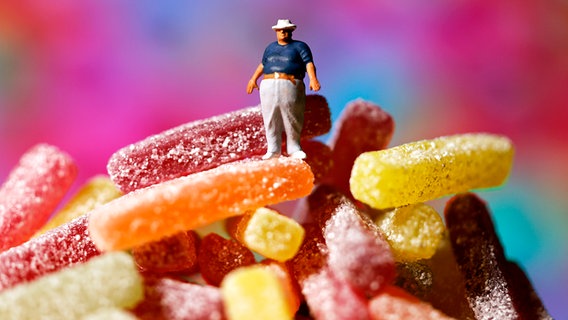 Auf einem Berg Süßigkeiten steht eine übergewichtige Männerfigur (Fotomontage) © picture alliance Foto: Christop Hardt
