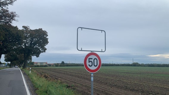 Von einem Ortsschild am Ortseingang Altentreptow ist nur noch der Rahmen übrig, durch den der bläulich-graue Morgenhimmel schimmert. Im Hintergrund ist vor allem Ackerland zu sehen. © NDR Foto: Claudia Arlt