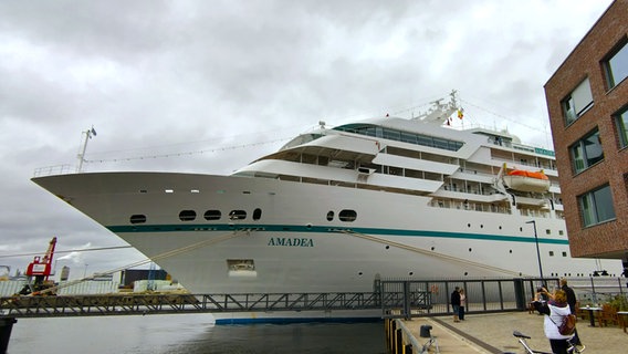 Die Spitze des Kreuzfahrtschiffes MS Amadea lugt hinter einem Haus im Wismarer Hafen hervor. Eine Frau fotografiert es. © NDR Foto: Christoph Woest