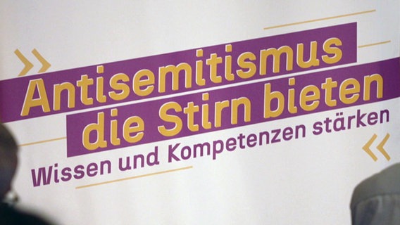 Auf eine Leinwand ist der Schriftzug "Antisemitismus die Stirn bieten - Wissen und Kompetenzen stärken" projeziert. © NDR Foto: NDR