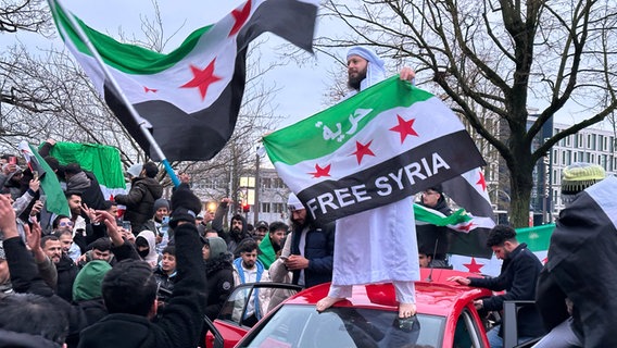 Rostock: Menschen feiern mit Fahnen den Sturz des Machthabers Assad in Syrien. © dpa Foto: Christopher Hirsch