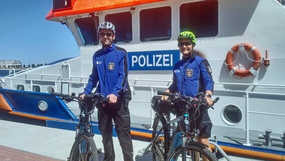 Uniformierte Polizisten im Bäderdienst stehen mit Fahrrädern vor einem Polizeischiff. © NDR Foto: Max Fuhrmann