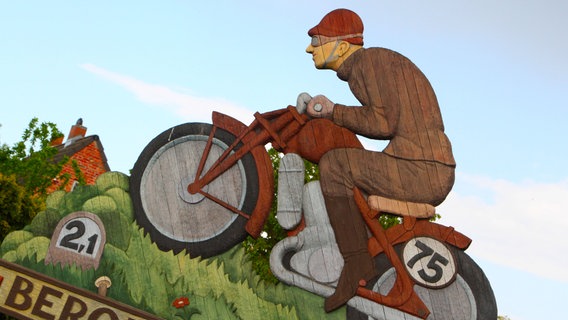 Blick auf eine Holzskulptur in Teterow am örtlichen Carl-Schröder-Platz, der Zufahrtsstraße zum Bergring, die einen Rennfahrer symbolisiert. © IMAGO / BildFunkMV 