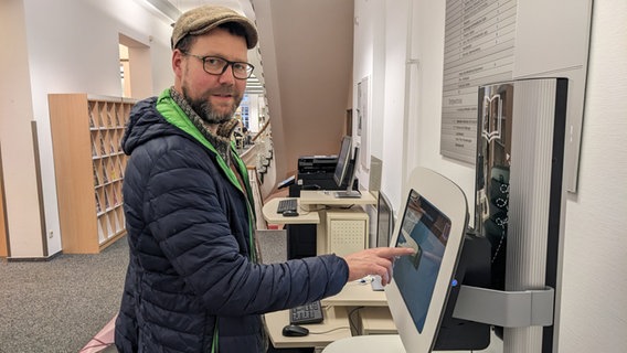 Ein Mann steht an einem Bildschirm und tippt mit dem Zeigefinger auf die Oberfläche. © Katja Bülow Foto: Katja Bülow