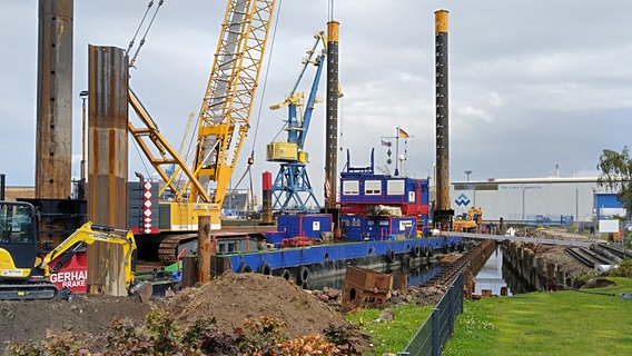 Kran, Bagger und anderes Baugerät baut an einer Wasserspundwand. © NDR Foto: Christoph Woest