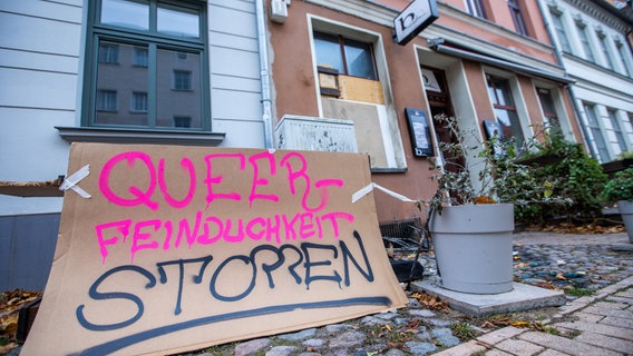 Ein Schild mit der Aufschrift "Queen Feindlichkeit stoppen" steht vor der Queer-Bar B 7 nach einem mutmaßlichen Brandanschlag. Nach einem mutmaßlichen Brandanschlag auf eine bei queeren Menschen beliebte Bar ermittelt die Kriminalpolizei wegen schwerer Brandstiftung © dpa Bildfunk Foto: Jens Büttner