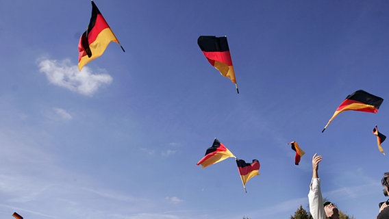 Tag der Deutschen Einheit 2007 in Schwerin: Fahnenträger werfen während der "Deutschlandparade" Nationalfahnen in die Luft. © Jens Büttner dpa/lmv Foto: Jens Büttner