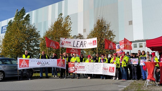 Etwa 50 Gewerkschaftler stehen mit Bannern auf einem Parkplatz vor der Wismarer Werfthalle. © NDR Foto: Christoph Woest