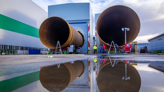 Monteure arbeiten an riesigen Metallrohren für Fundamente von Off-Shore-Windkraftanlagen, die im Großrohrwerk EEW Special Pipe Constructions im Seehafen gebaut werden. © picture alliance/dpa Foto: Jens Büttner