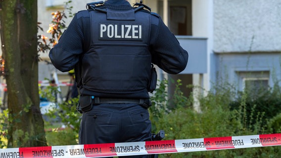 Ein Polizist steht hinter einem Absperrband hängt im Stadtteil Knieper West. © Stefan Sauer/dpa +++ dpa-Bildfunk +++ Foto: Stefan Sauer/dpa +++ dpa-Bildfunk +++