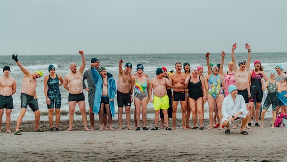 Eine Gruppe von Menschen steht bei kalten Temperaturen in Badekleidung am Strand. © Eisbademeisters Rostock Foto: David Garbe